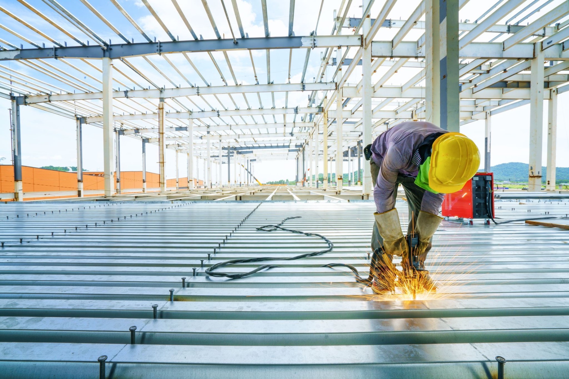 Worker welding the steel structure of a large industrial building — symbol of heavy material decarbonization