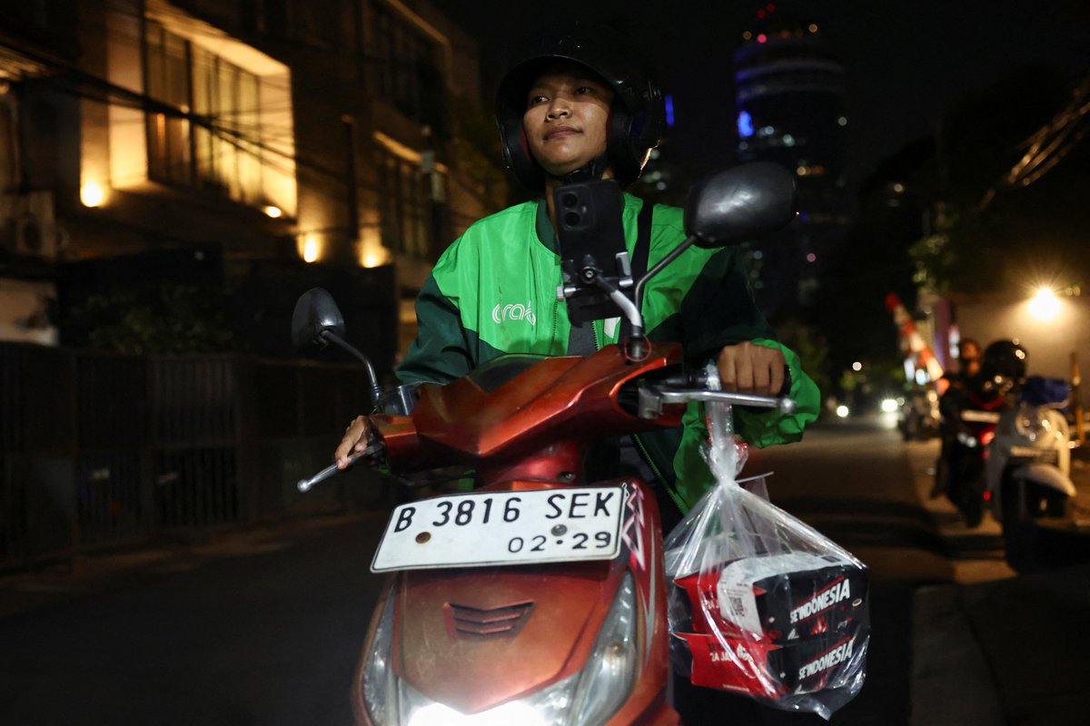Last-mile delivery rider on a motorbike carrying a parcel through a city at night — Scope 3.9 downstream transport and distribution